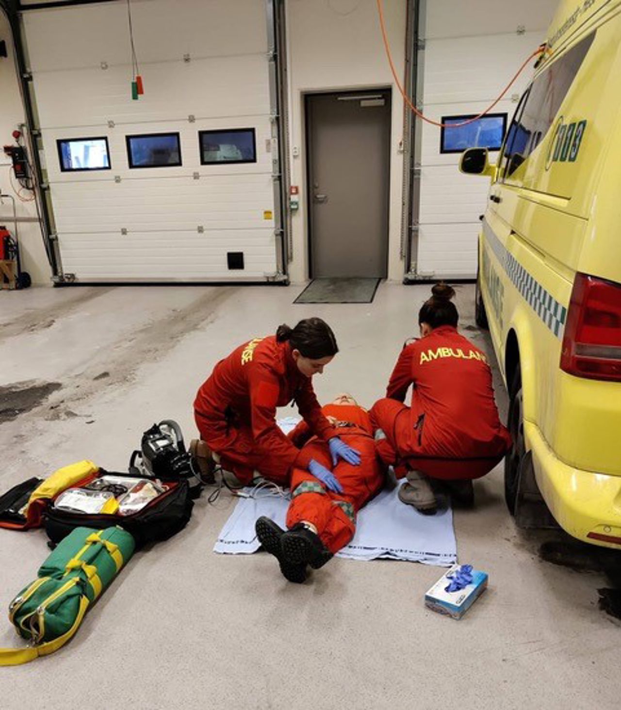Bilete viser to personar som sit med ein pasient ved sida av ein ambulanse